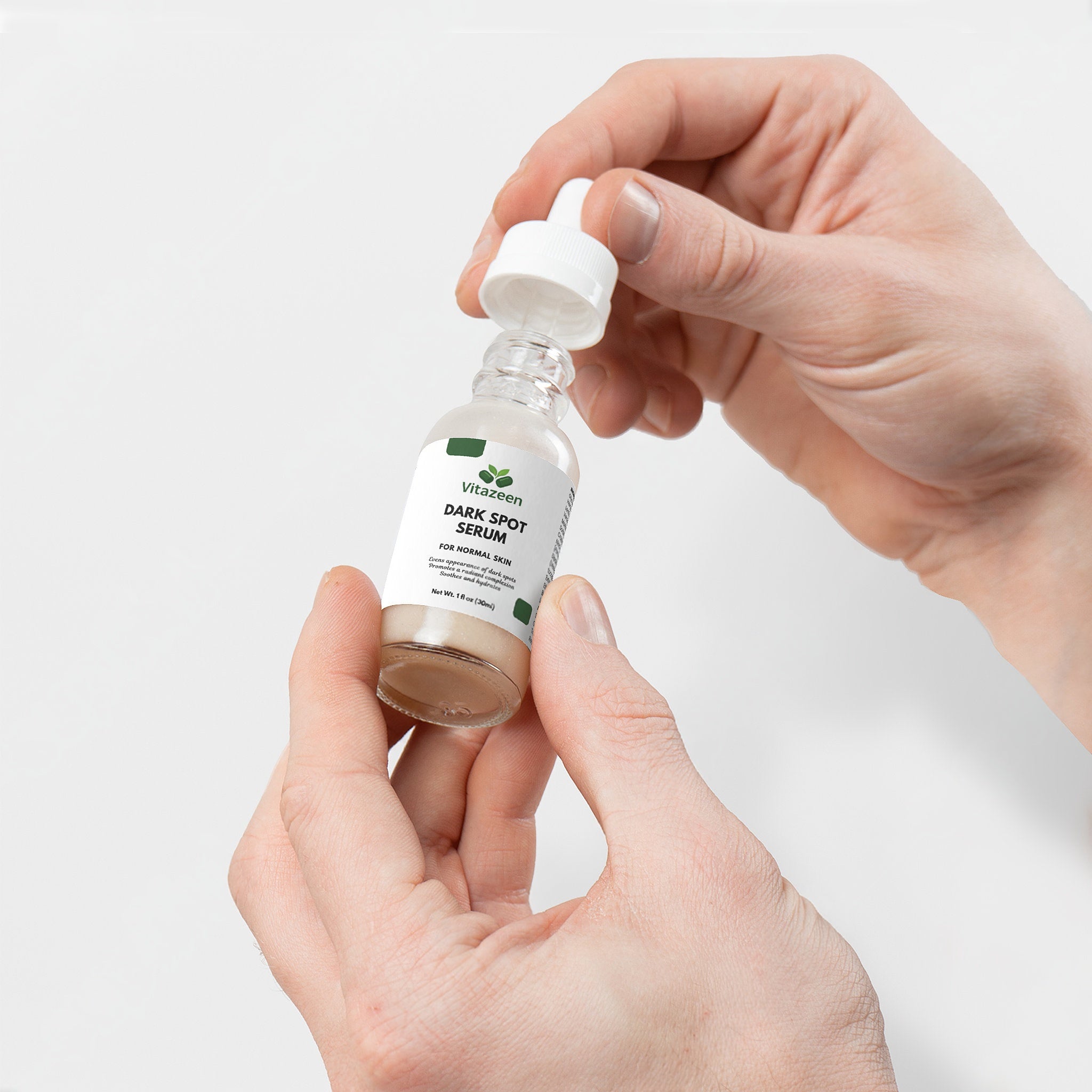 Hand holding a bottle of dark spot serum with a white background